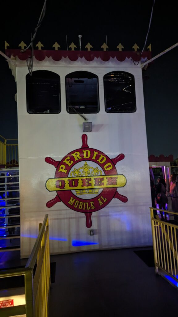 The Perdido Queen dinner cruise ship’s cabin section, displaying its logo, with dining and entertainment areas visible on the upper levels.