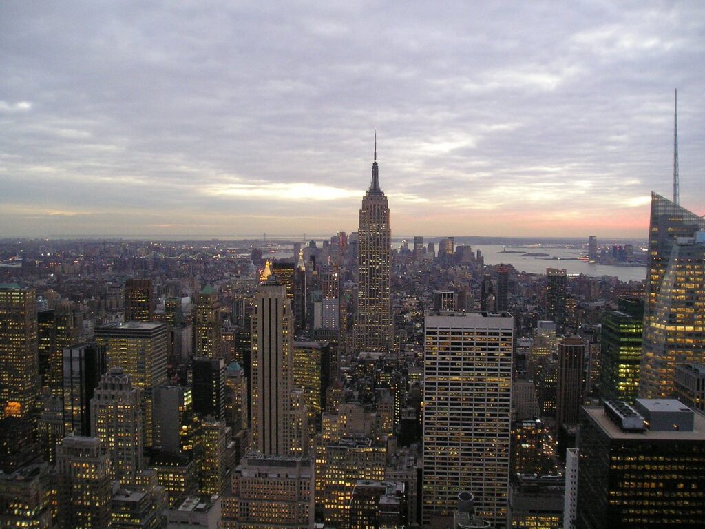 Number 4 of the top 5 travel destinations, an aerial view of Manhattan in the evening, illuminated by vibrant city lights, with skyscrapers towering over the bustling streets below.