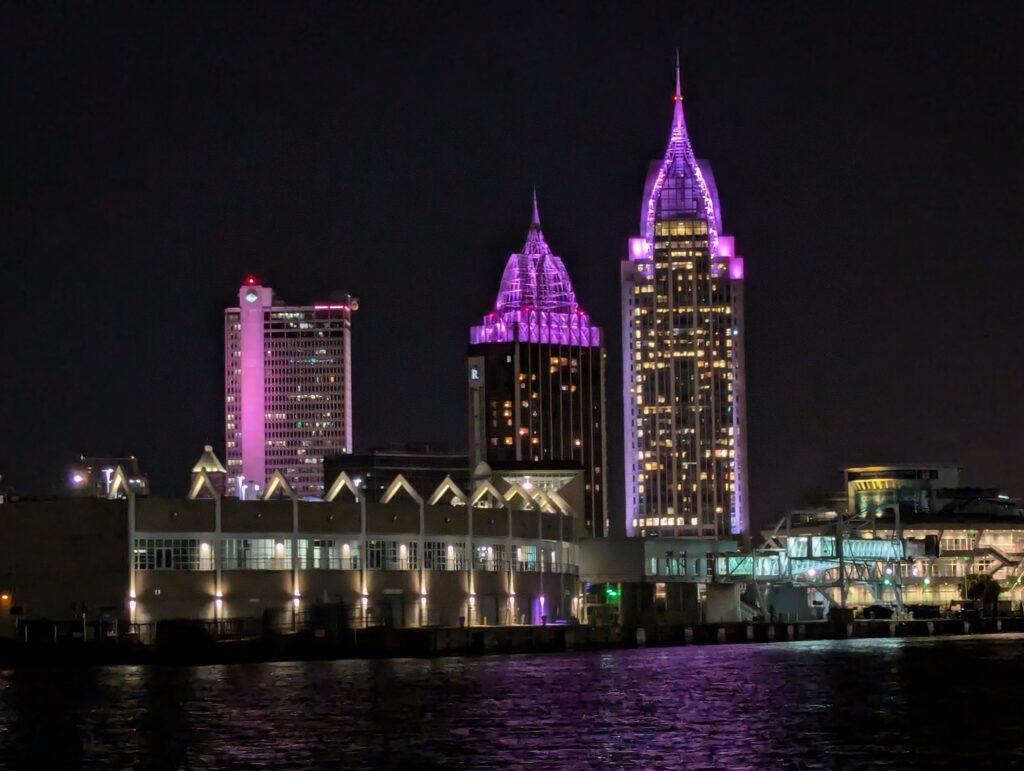 The glowing city lights of Mobile, Alabama, as seen from the deck of the Perdido Queen dinner cruise ship at night.