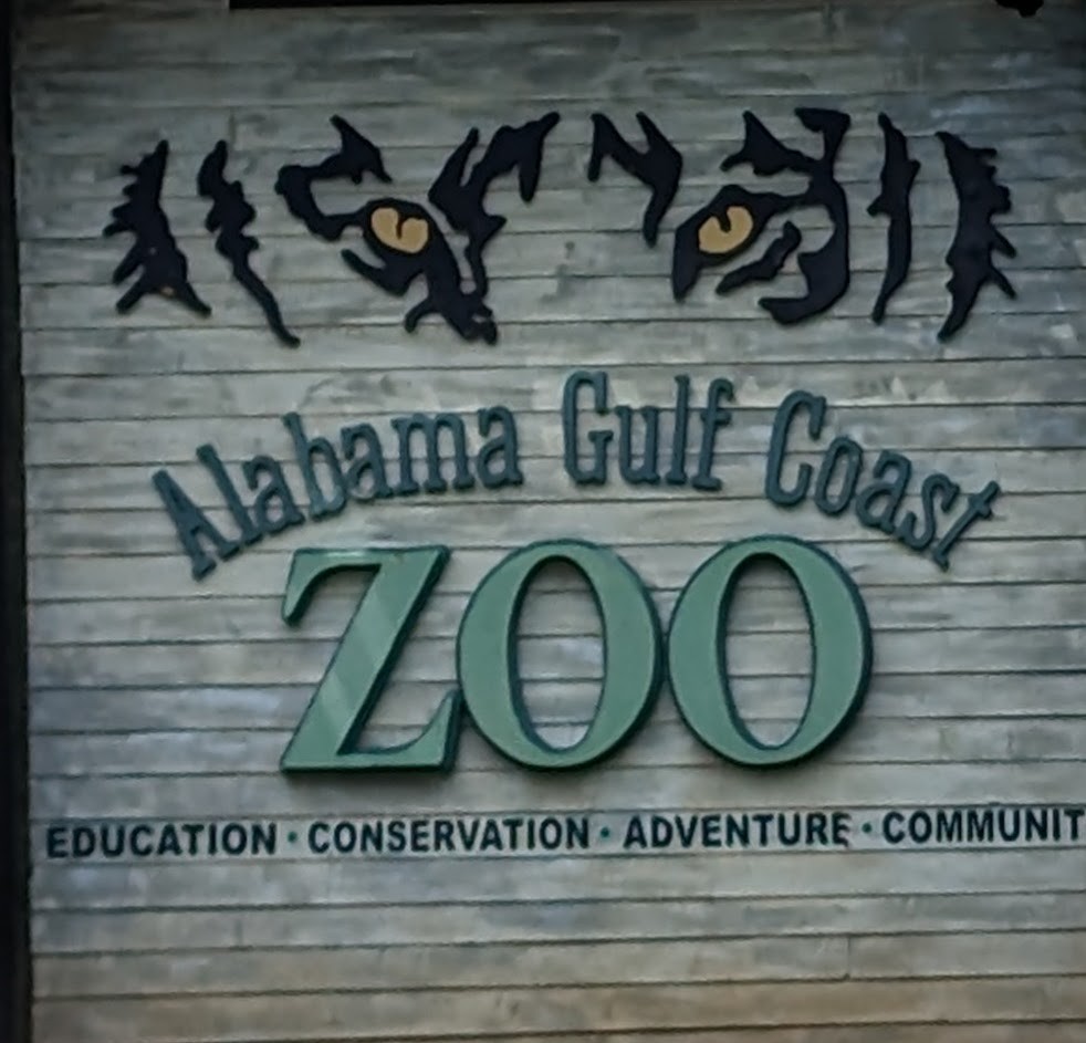 Entrance sign to the Alabama Gulf Coast Zoo in Gulf Shores, Alabama, surrounded by lush greenery.